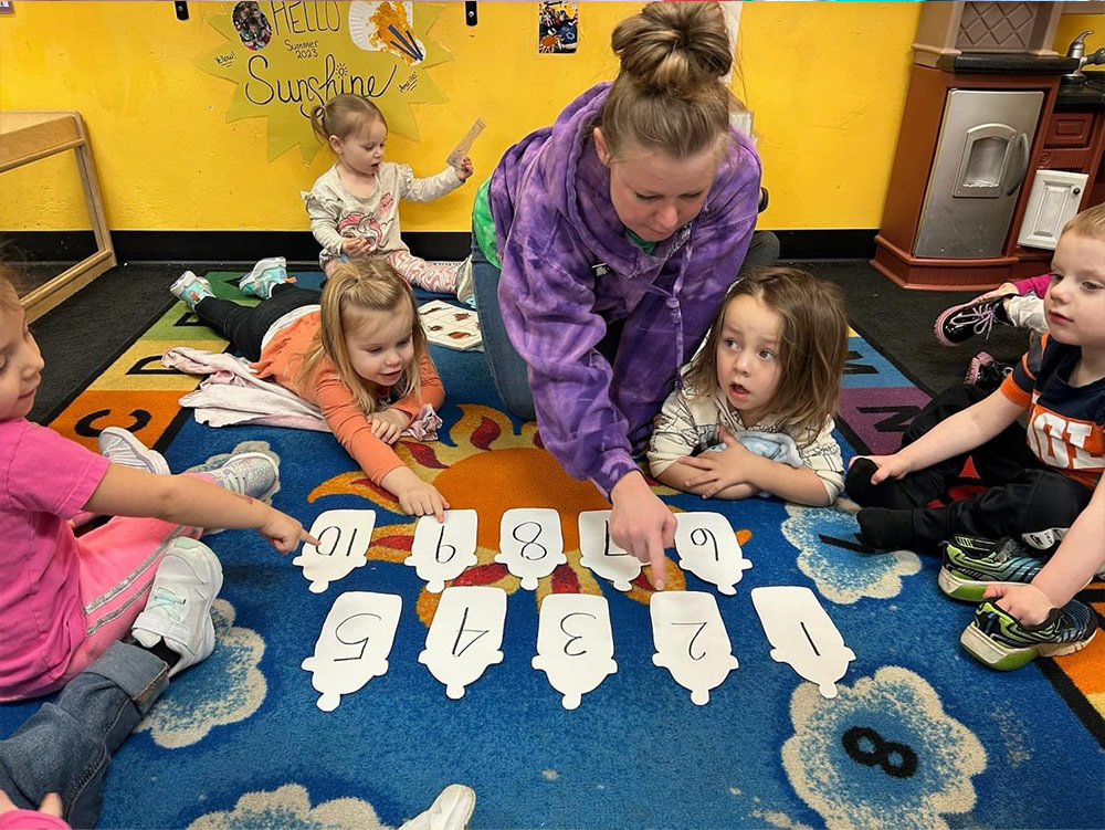 2-Year-Old Room - teacher with 2-year-olds showing a tomato at Robins Nest Learning Center