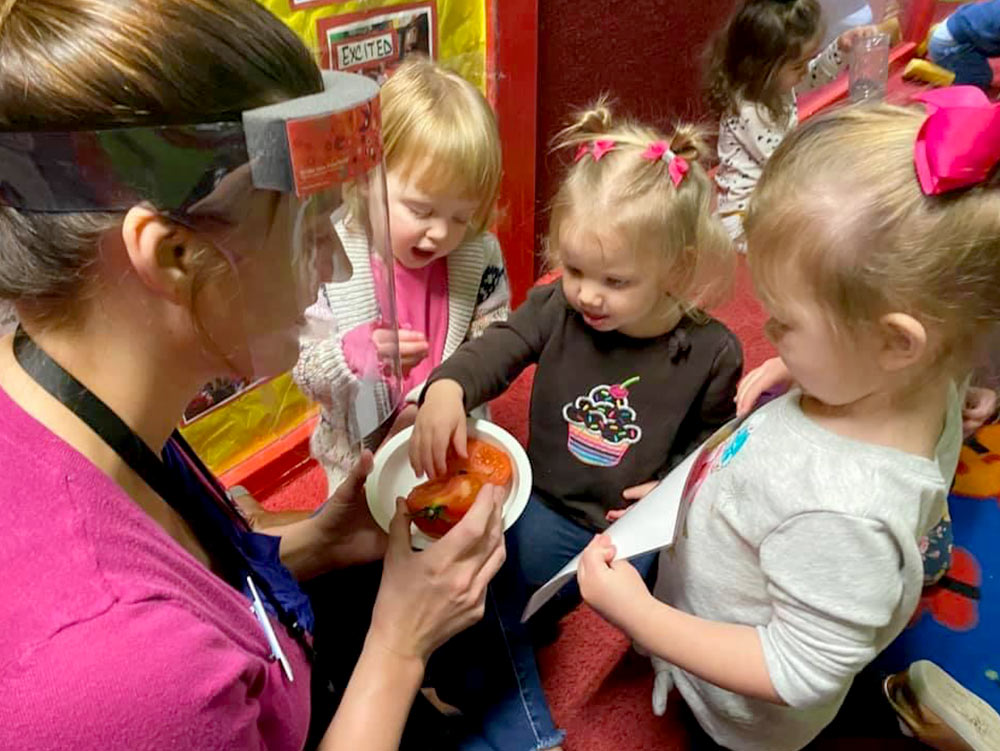 2-Year-Old Room - teacher with 2-year-olds showing a tomato at Robins Nest Learning Center