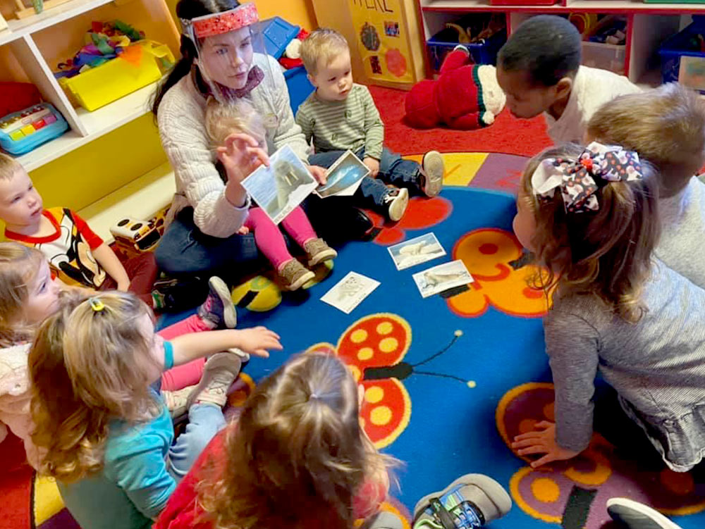 2-Year-Old Room - teacher with 2-year-olds on carpet at Robins Nest Learning Center